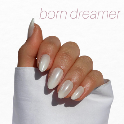An elegantly manicured hand displays iridescent, pearl-like French tips from the Bridal Bliss Collection by Glowie By Her (20% Off) against a white background. "Born dreamer" is written in muted pink at the top.