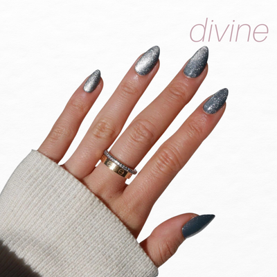 A cream sleeve partially covers a hand adorned with almond-shaped, chrome glitter nails and two gold rings. "Divine" appears in light pink on the white background, reflecting the elegance of Glowie By Her's Glam Night Out collection (20% Off).