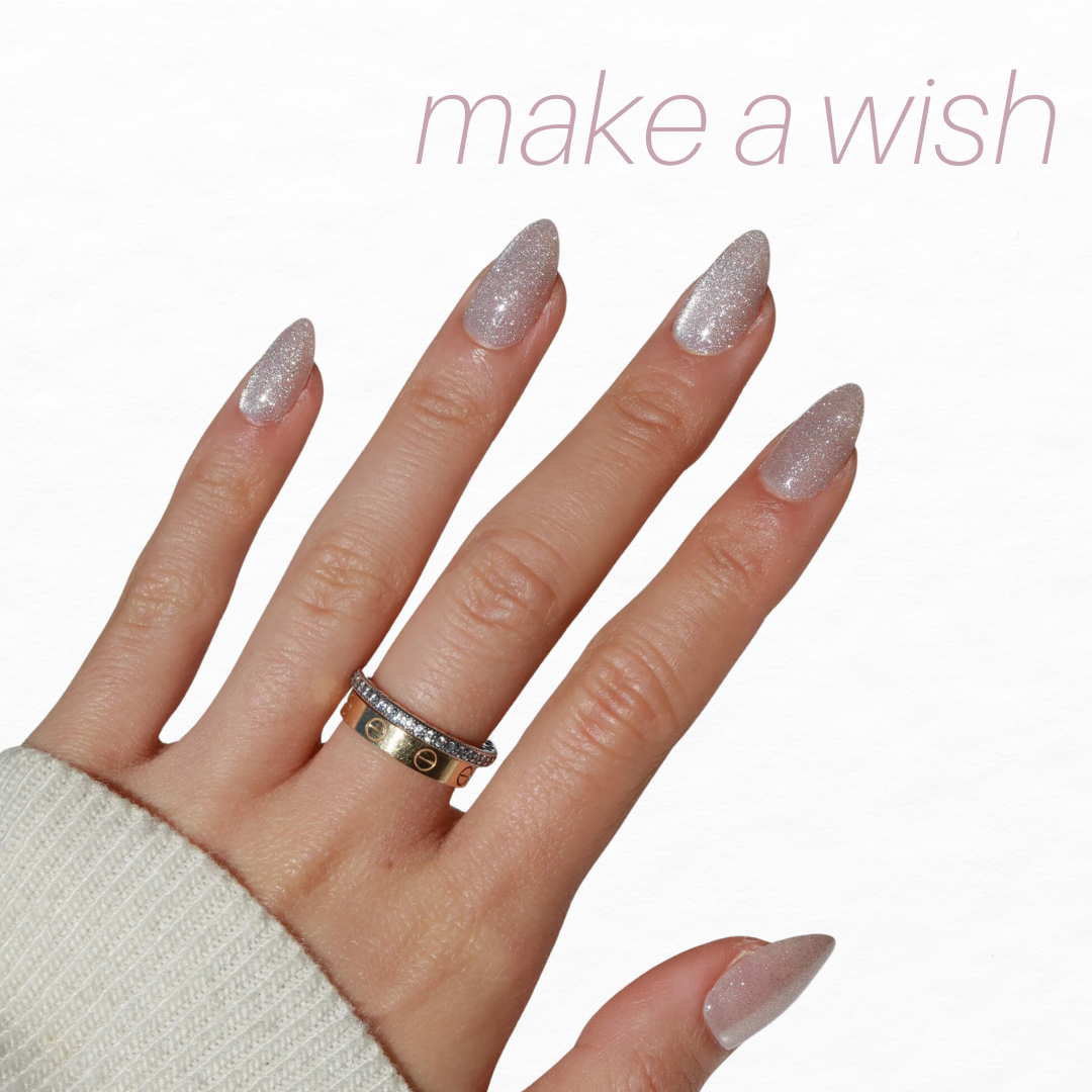 A hand flaunts almond-shaped, glittery nails from Glowie By Her's Glam Night Out (20% Off) collection. Two rings—one plain and another with small diamonds—adorn the fingers against a white background, while "Make a wish" appears in light pink at the top right corner.